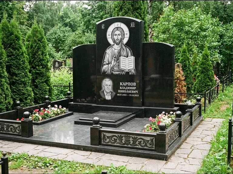 Памятник с гравировкой иконы: широкая панорамная стела с золочёным нимбом — гравировка образа Матроны Московской, цветник с белыми хризантемами, работа «Мельникова» в Ульяновске