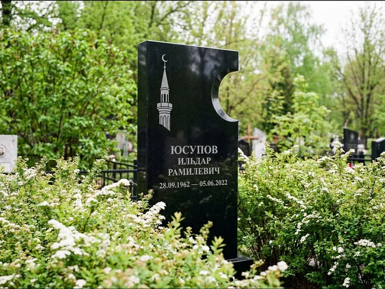 Мусульманский памятник с гравировкой мечети: стела с боковым вырезом в форме полумесяца — гравировка минарета с полумесяцем, низкие кусты спиреи в цвету, работа «Юсупов» в Ульяновске